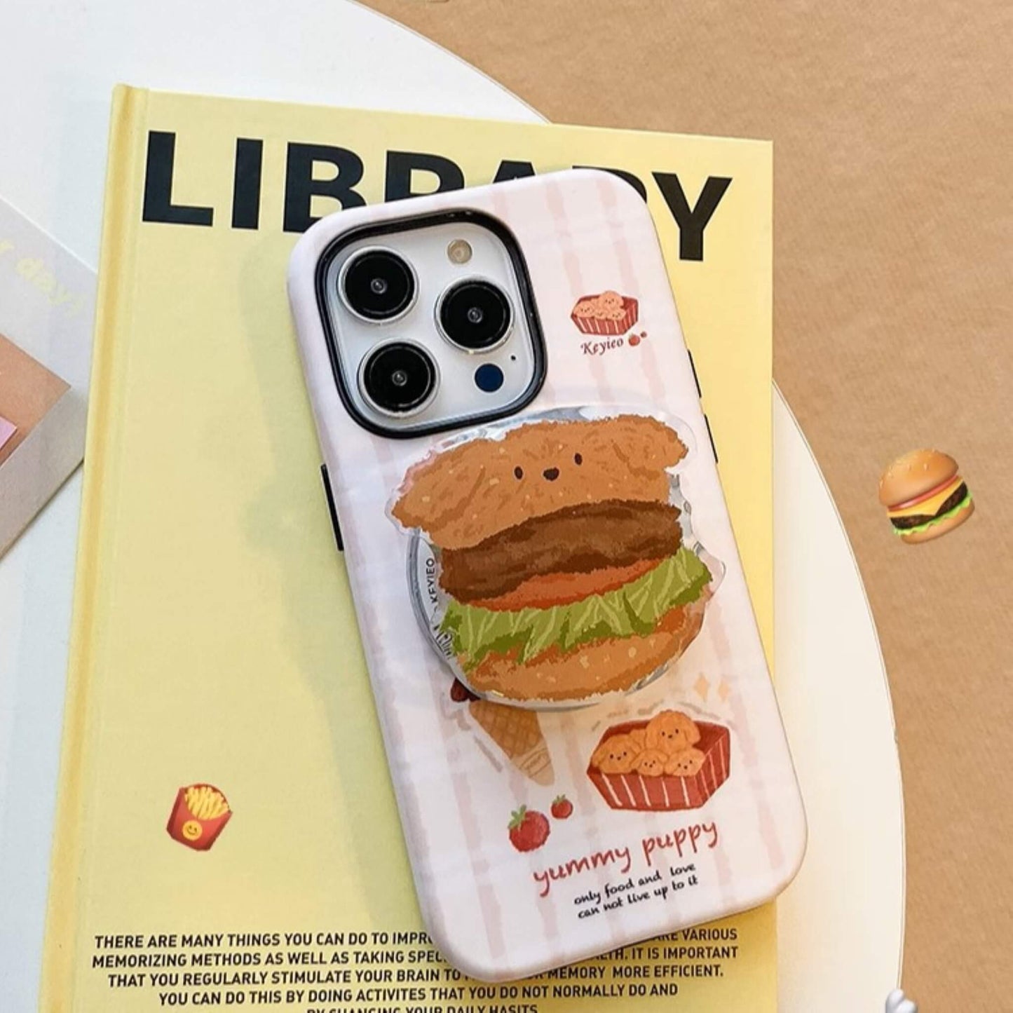 Cute phone case with a unique 'yummy puppy' design, featuring delightful snack-themed illustrations, compatible with MagSafe accessories, displayed next to a burger-shaped MagSafe popsocket. With MagSafe Popsocket Attached.