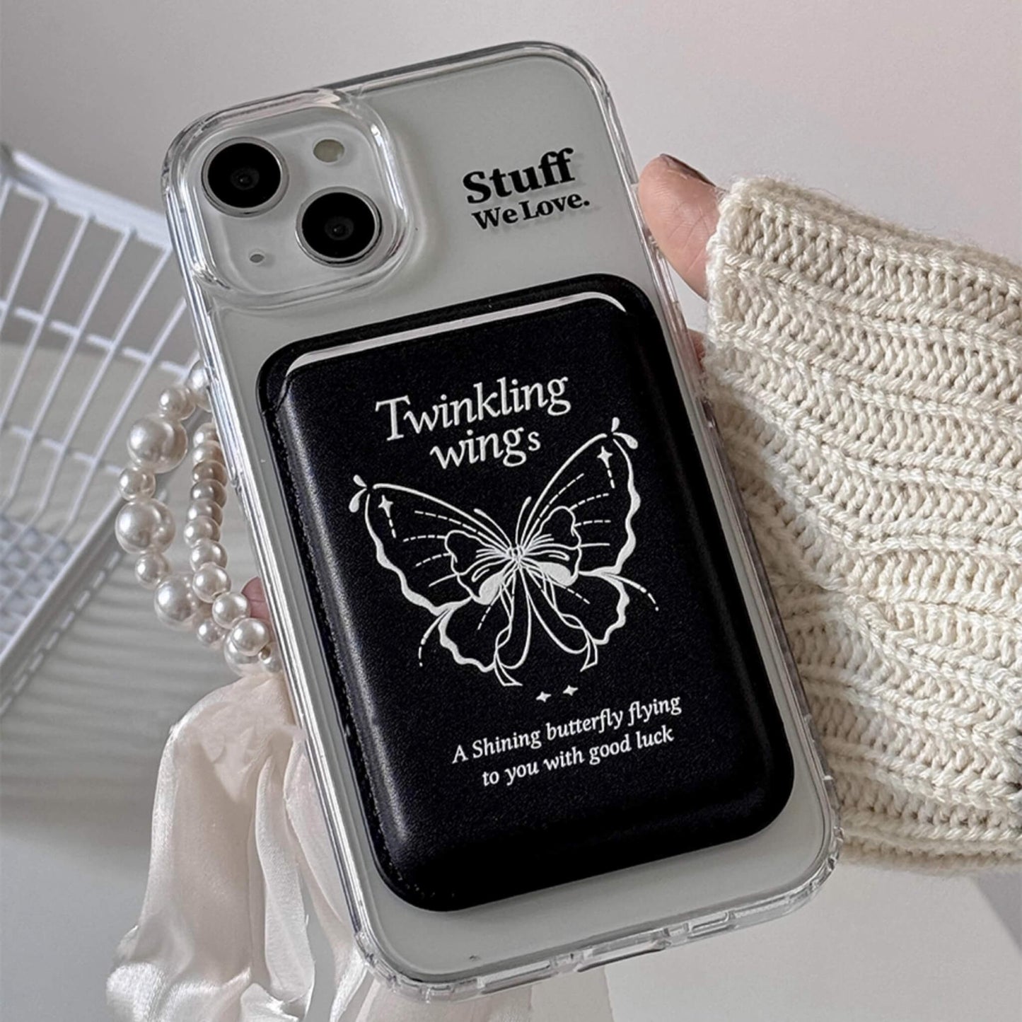 Black MagSafe phone cases, attached by Magsafe wallet with black based and reach with an embossed butterfly and 'Twinkling wings' text, symbolizing good luck, set against a clear case background