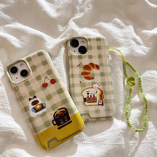 A duo of Cozy Café Critters iphone cases with card holder slot, featuring charming animal designs and a checkered pattern, accompanied by a fresh green beaded phone strap, all laid out on a textured white fabric