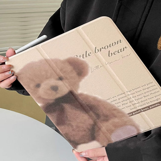 "Beige iPad case with a vintage teddy bear design and scripted text, displayed next to a white ceramic mug. Acrylic clear back with a slot for Apple Pencil."